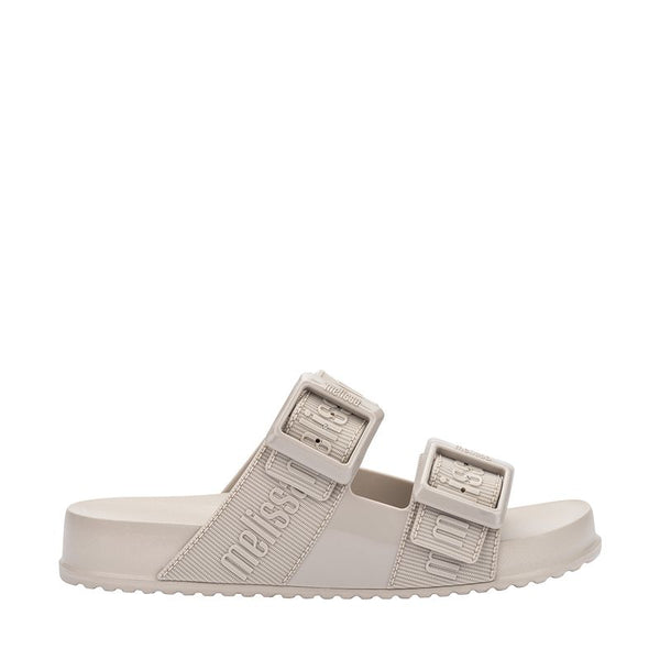 Chinelo adulto Melissa Cozy Slide M.Lover na cor bege claro, com duas tiras largas ajustáveis com fivelas e logo em relevo. Fabricado em Melflex, com solado tratorado e palmilha anatômica. Ideal para quem busca conforto, praticidade e estilo clean no dia a dia.
