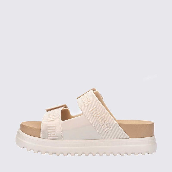 Sandália plataforma Melissa Cozy M.Lover na cor bege, com duas tiras largas ajustáveis com fivelas e logo em relevo. Confeccionada em Melflex, possui solado tratorado e palmilha anatômica, unindo conforto e estilo em um design moderno para looks casuais."