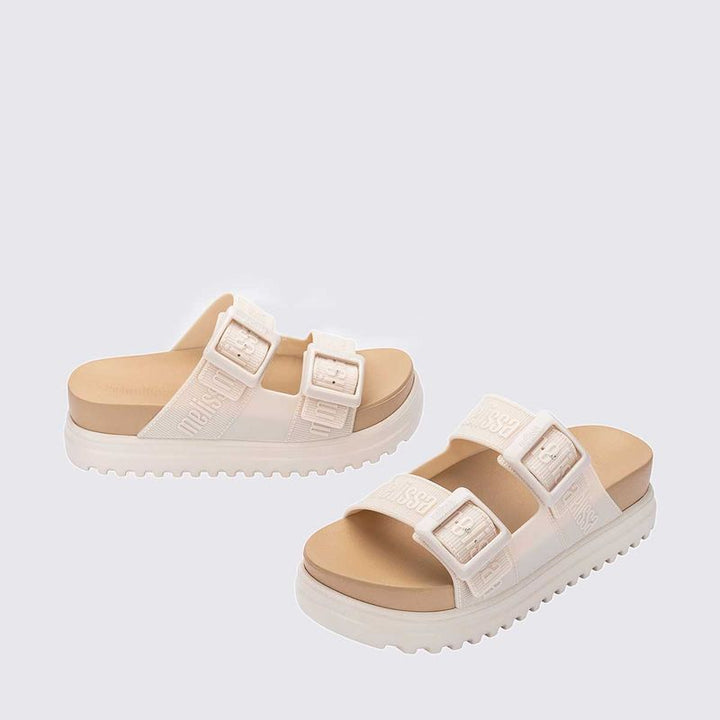 Sandália plataforma Melissa Cozy M.Lover na cor bege, com duas tiras largas ajustáveis com fivelas e logo em relevo. Confeccionada em Melflex, possui solado tratorado e palmilha anatômica, unindo conforto e estilo em um design moderno para looks casuais."