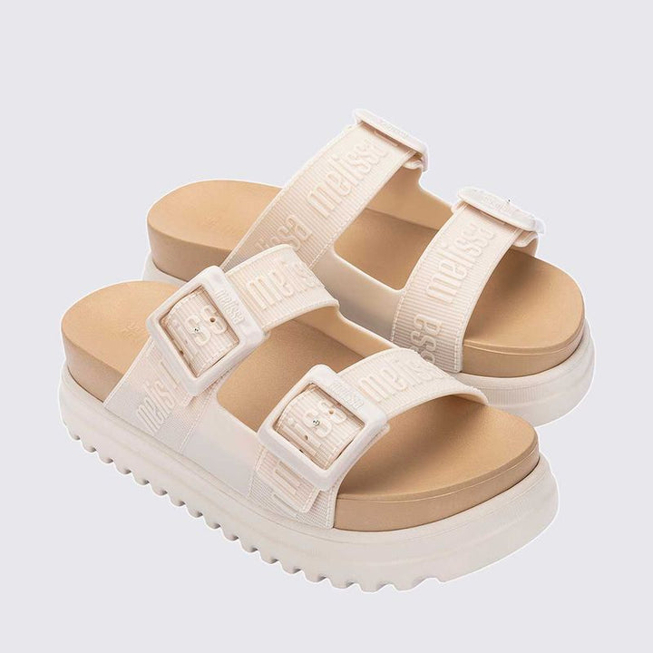 Sandália plataforma Melissa Cozy M.Lover na cor bege, com duas tiras largas ajustáveis com fivelas e logo em relevo. Confeccionada em Melflex, possui solado tratorado e palmilha anatômica, unindo conforto e estilo em um design moderno para looks casuais."