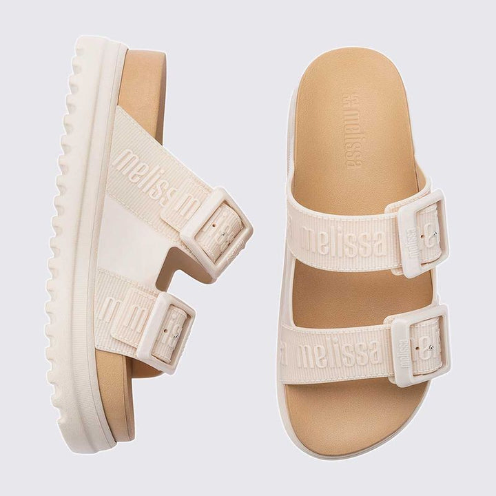 Sandália plataforma Melissa Cozy M.Lover na cor bege, com duas tiras largas ajustáveis com fivelas e logo em relevo. Confeccionada em Melflex, possui solado tratorado e palmilha anatômica, unindo conforto e estilo em um design moderno para looks casuais."