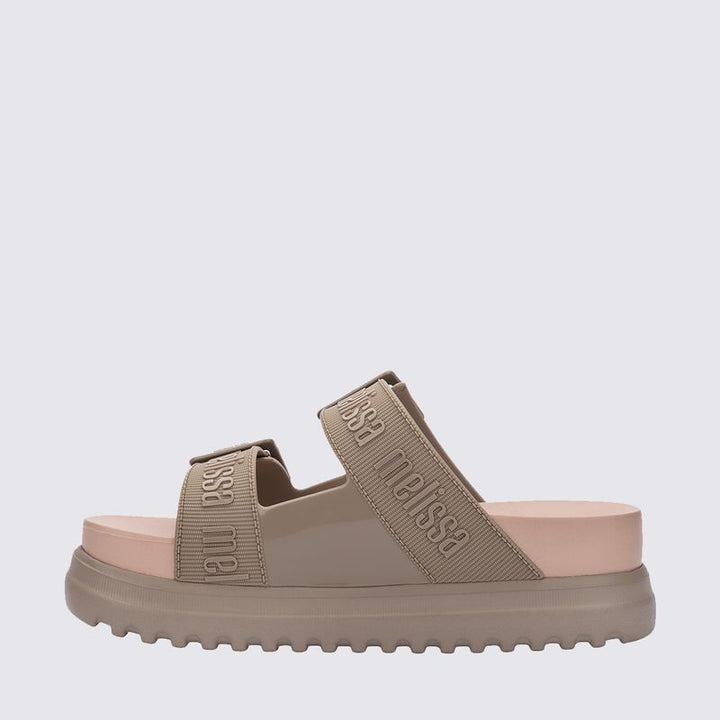 Sandália plataforma Melissa Cozy M.Lover na cor bege médio, com duas tiras largas ajustáveis com fivelas e logo Melissa em relevo. Produzida em Melflex, possui solado alto tratorado e palmilha anatômica, unindo conforto, estilo e praticidade em um visual moderno