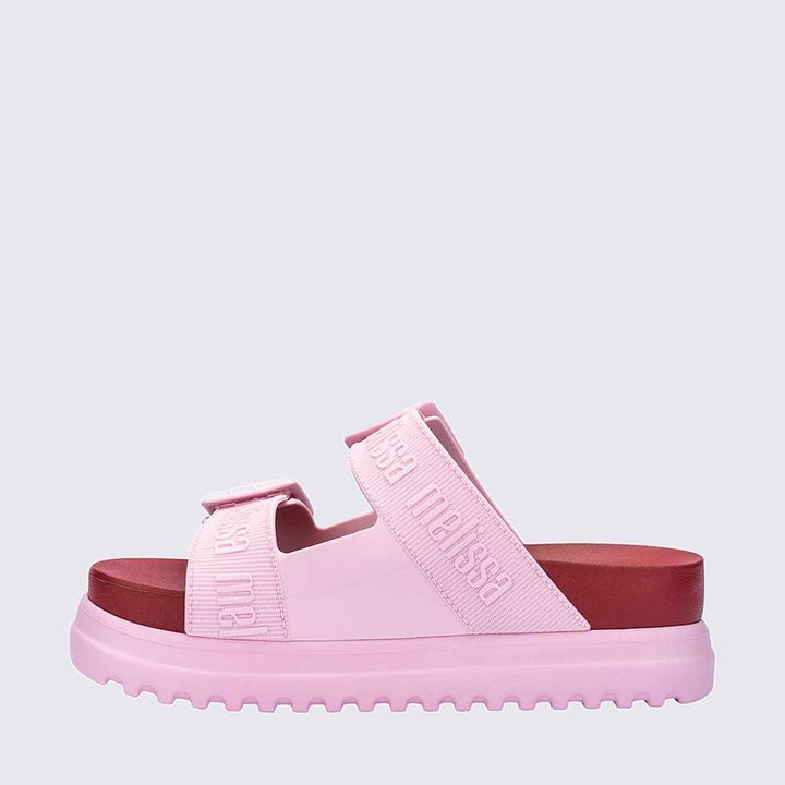Sandália plataforma adulta Melissa Cozy M.Lover nas cores rosa e vermelho, com duas tiras largas ajustáveis com fivelas e logo em relevo. Produzida em Melflex, com solado tratorado alto e palmilha anatômica, combina conforto, estilo marcante e atitude nos looks casuais