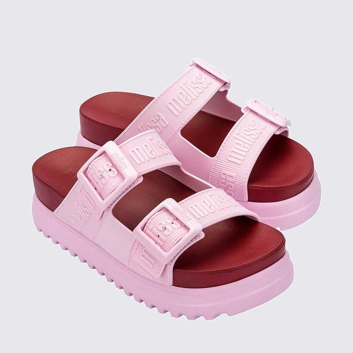 Sandália plataforma adulta Melissa Cozy M.Lover nas cores rosa e vermelho, com duas tiras largas ajustáveis com fivelas e logo em relevo. Produzida em Melflex, com solado tratorado alto e palmilha anatômica, combina conforto, estilo marcante e atitude nos looks casuais