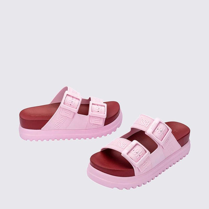 Sandália plataforma adulta Melissa Cozy M.Lover nas cores rosa e vermelho, com duas tiras largas ajustáveis com fivelas e logo em relevo. Produzida em Melflex, com solado tratorado alto e palmilha anatômica, combina conforto, estilo marcante e atitude nos looks casuais