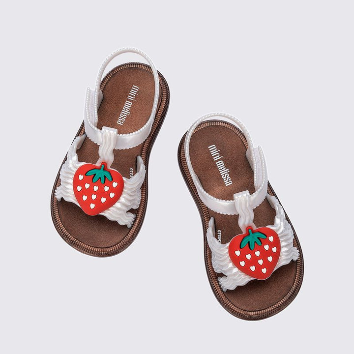 Sandália infantil Mini Melissa Hip Sandal Baby nas cores bronze e branco perolado, com tiras largas e fechamento em velcro. Produzida em Melflex, é leve, confortável e segura, perfeita para os primeiros passos com brilho delicado e muito estilo