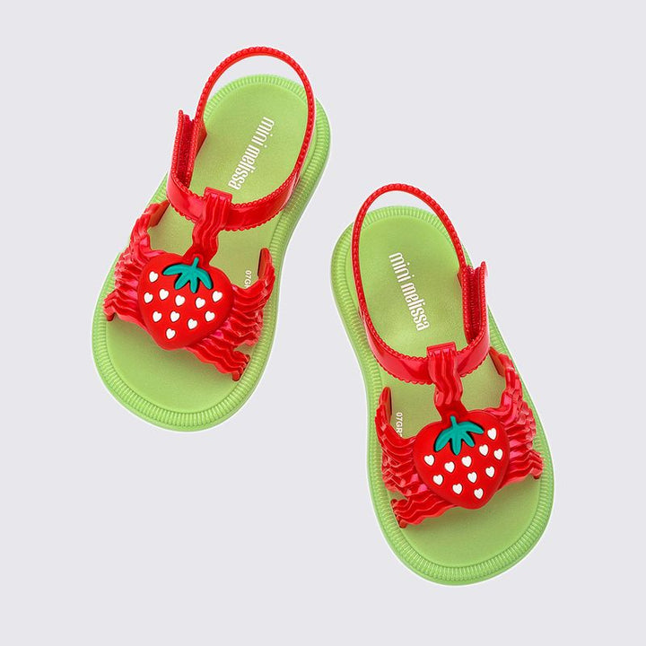 Sandália infantil Mini Melissa Hip Sandal Baby nas cores verde e vermelho, com tiras largas e fechamento em velcro. Confeccionada em Melflex, é leve, confortável e segura, ideal para acompanhar os primeiros passos com estilo divertido e prático