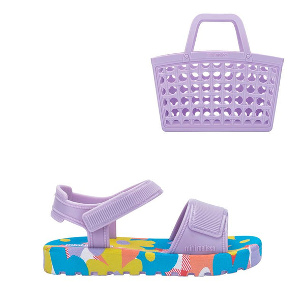 Mini Melissa + Bolsa Imagine Baby Lilás Azul, com acabamento brilhante e translúcido. Feita em material Melflex, possui design moderno com tiras largas cruzadas sobre o pé e fechamento prático ajustável. Solado rasteiro, leve e confortável, perfeito para criar looks casuais e estilosos para o dia a dia. Acompanha uma bolsa lilas de 5 litros, ideal para carregar seus itens com praticidade e estilo.