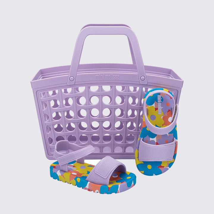Mini Melissa + Bolsa Imagine Baby Lilás Azul, com acabamento brilhante e translúcido. Feita em material Melflex, possui design moderno com tiras largas cruzadas sobre o pé e fechamento prático ajustável. Solado rasteiro, leve e confortável, perfeito para criar looks casuais e estilosos para o dia a dia. Acompanha uma bolsa lilas de 5 litros, ideal para carregar seus itens com praticidade e estilo.