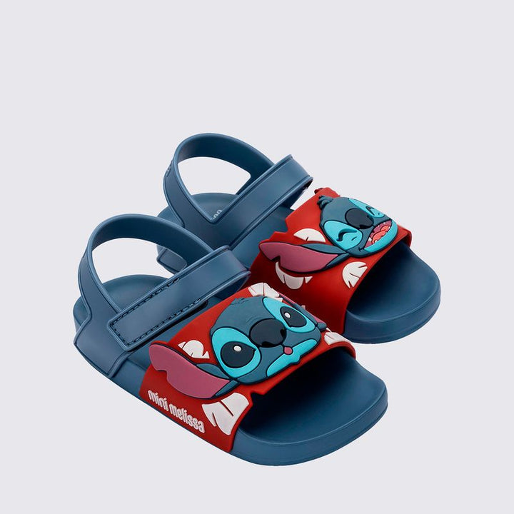 Sandália infantil Mini Melissa Flowing Sandal Stitch Baby nas cores azul e vermelho, com aplique do personagem Stitch na parte frontal. Feita em Melflex, possui tiras largas, fechamento em velcro e solado confortável, perfeita para os pequenos fãs da Disney