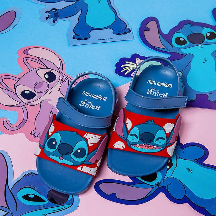 Sandália infantil Mini Melissa Flowing Sandal Stitch Baby nas cores azul e vermelho, com aplique do personagem Stitch na parte frontal. Feita em Melflex, possui tiras largas, fechamento em velcro e solado confortável, perfeita para os pequenos fãs da Disney