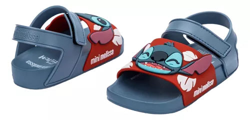 Sandália infantil Mini Melissa Flowing Sandal Stitch Baby nas cores azul e vermelho, com aplique do personagem Stitch na parte frontal. Feita em Melflex, possui tiras largas, fechamento em velcro e solado confortável, perfeita para os pequenos fãs da Disney