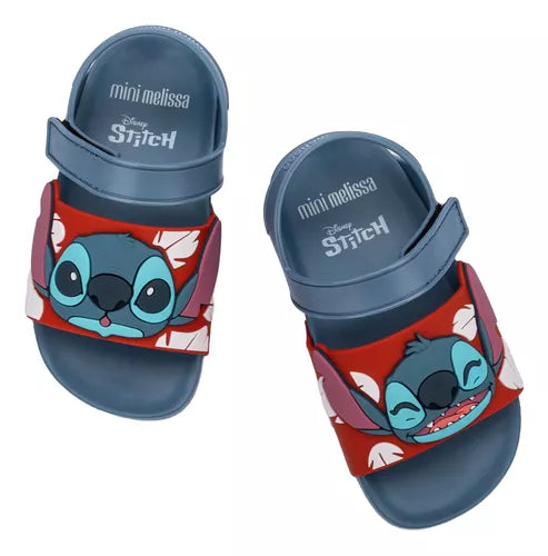 Sandália infantil Mini Melissa Flowing Sandal Stitch Baby nas cores azul e vermelho, com aplique do personagem Stitch na parte frontal. Feita em Melflex, possui tiras largas, fechamento em velcro e solado confortável, perfeita para os pequenos fãs da Disney