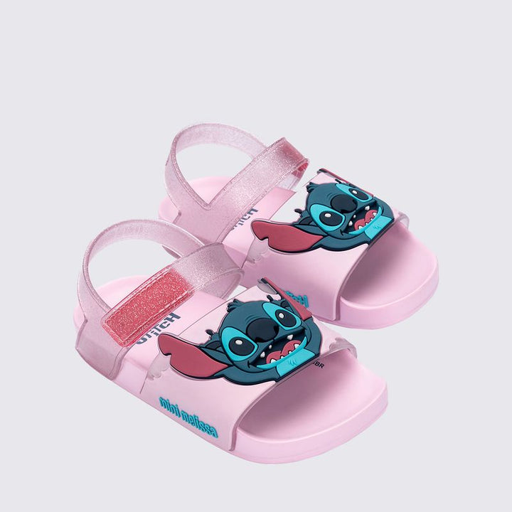 Sandália infantil Mini Melissa Flowing Sandal Stitch Baby nas cores rosa e azul, com aplique do personagem Stitch no cabedal. Produzida em Melflex, conta com tiras largas, solado confortável e fecho em velcro. Ideal para os pequenos que amam Disney com muito estilo e praticidade