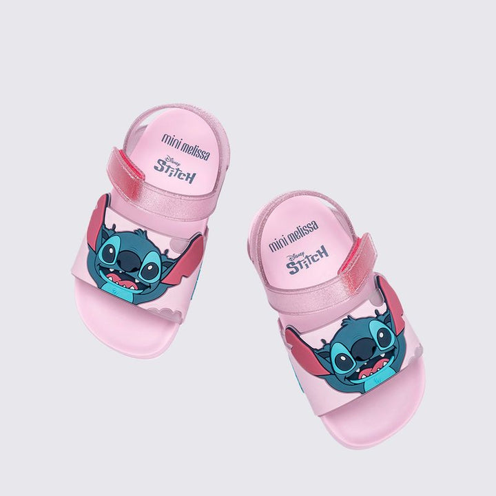Sandália infantil Mini Melissa Flowing Sandal Stitch Baby nas cores rosa e azul, com aplique do personagem Stitch no cabedal. Produzida em Melflex, conta com tiras largas, solado confortável e fecho em velcro. Ideal para os pequenos que amam Disney com muito estilo e praticidade