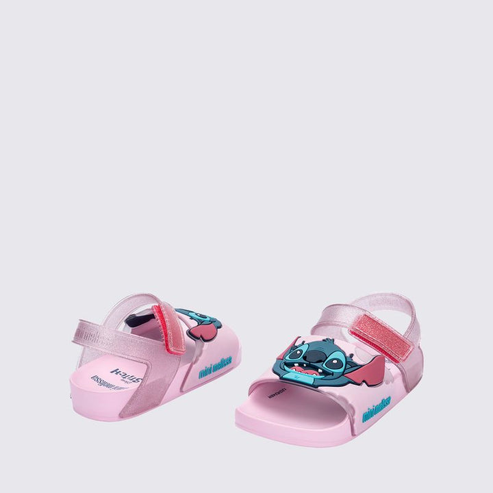 Sandália infantil Mini Melissa Flowing Sandal Stitch Baby nas cores rosa e azul, com aplique do personagem Stitch no cabedal. Produzida em Melflex, conta com tiras largas, solado confortável e fecho em velcro. Ideal para os pequenos que amam Disney com muito estilo e praticidade