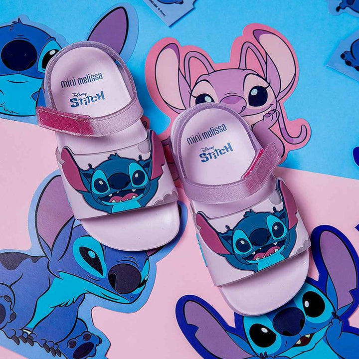 Sandália infantil Mini Melissa Flowing Sandal Stitch Baby nas cores rosa e azul, com aplique do personagem Stitch no cabedal. Produzida em Melflex, conta com tiras largas, solado confortável e fecho em velcro. Ideal para os pequenos que amam Disney com muito estilo e praticidade