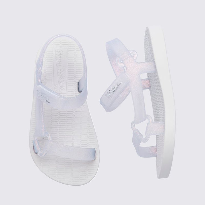 Sandália infantil Mini Melissa Sun Downtown Baby na cor branco com efeito vidro e glitter, acabamento brilhante e design unissex. Feita em Melflex, é leve, confortável e possui fechamento em velcro, garantindo segurança e estilo para os pequenos
